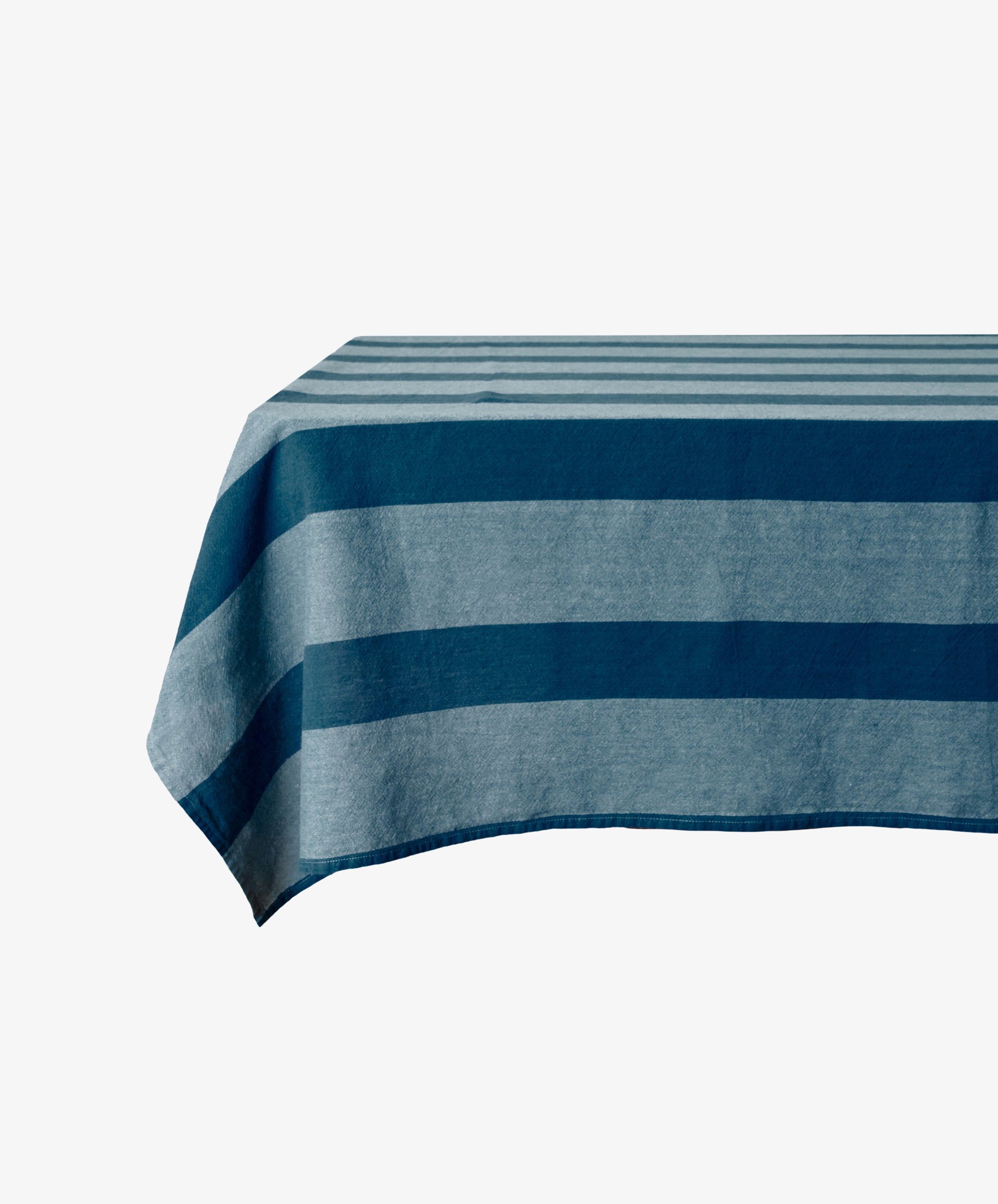 The Cruz Tablecloth, made from natural fibres, features blue and gray stripes and is displayed draped over a rectangular table against a plain white background.