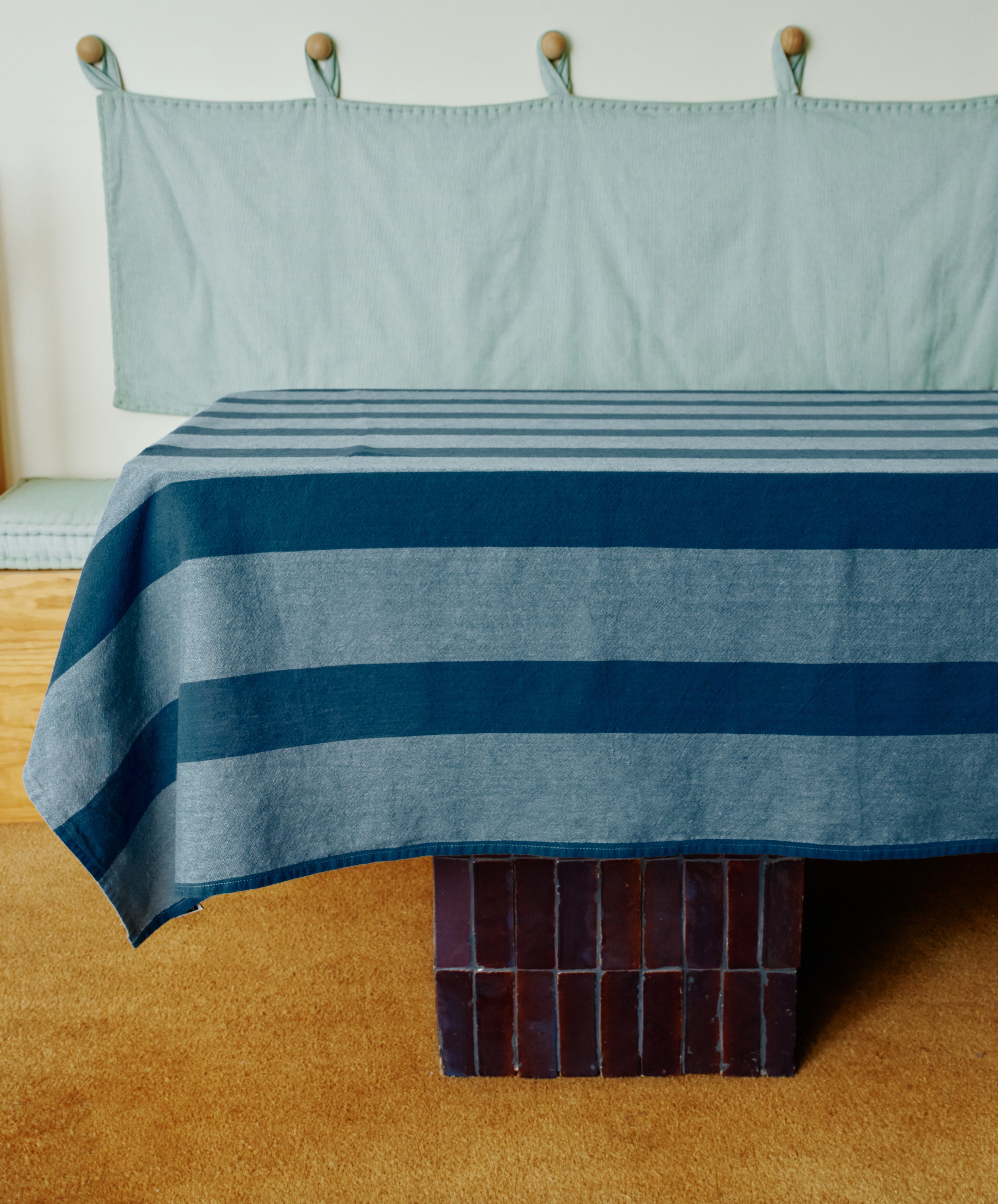 A table draped in the Cruz Tablecloth stands on a brown tile floor, complemented by a tan carpet and light blue fabric wall art, bringing the charm of natural fibres to the space.