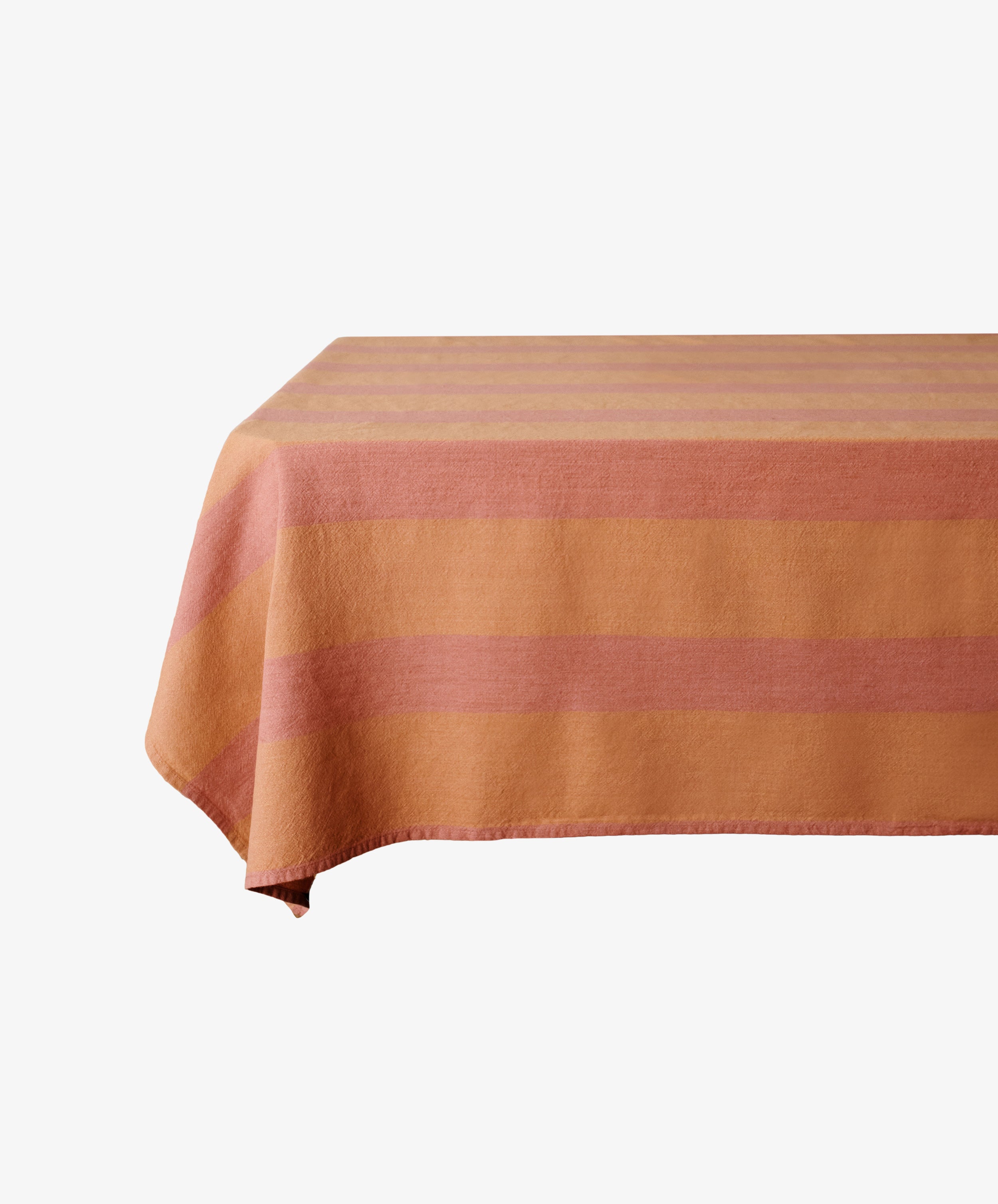 The Cruz Tablecloth, made of washed linen, features horizontal orange and pink stripes on a plain rectangular table.