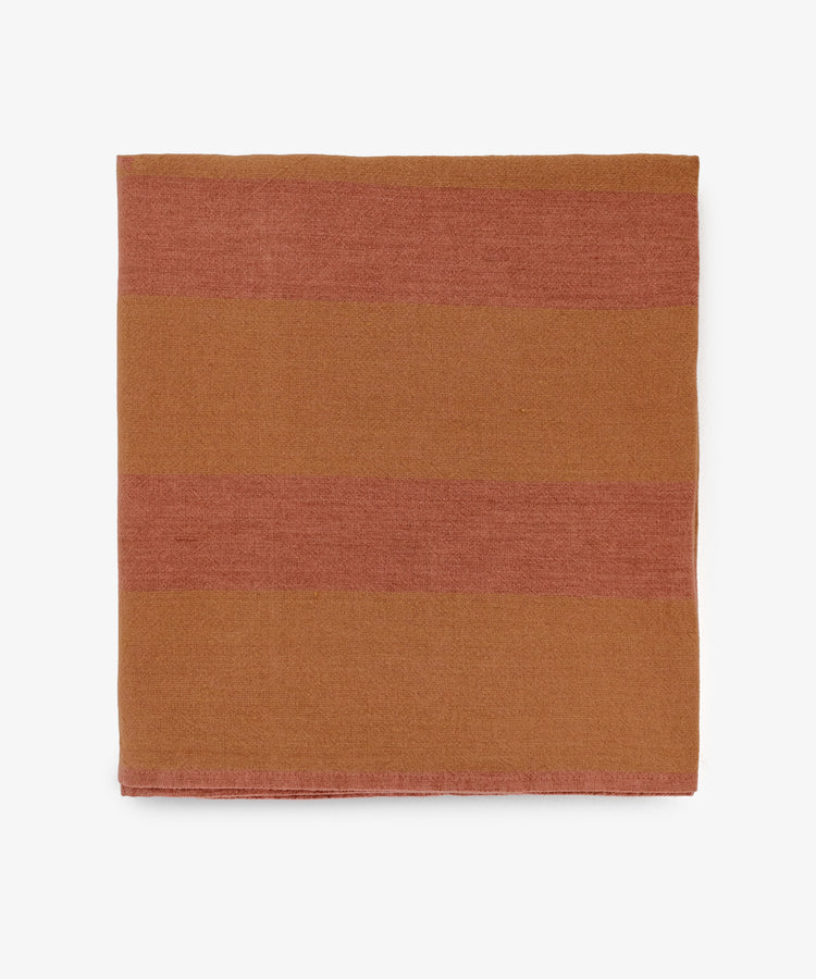 The Cruz Tablecloth is a folded, square linen featuring wide horizontal stripes in brown and rust on a white background.