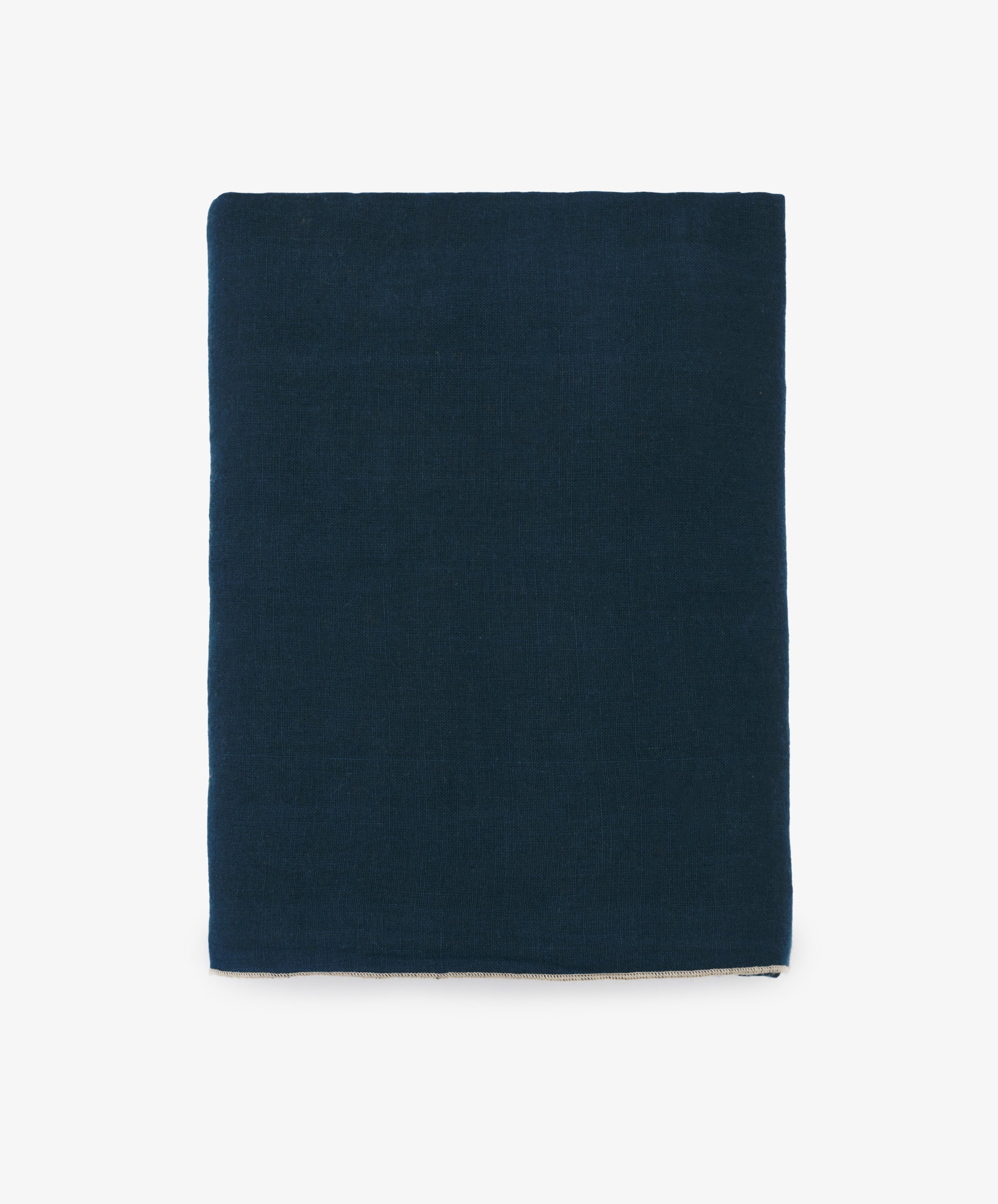 Venise Tablecloth. Folded rectangular dark blue linen cloth with cream stitched hem.