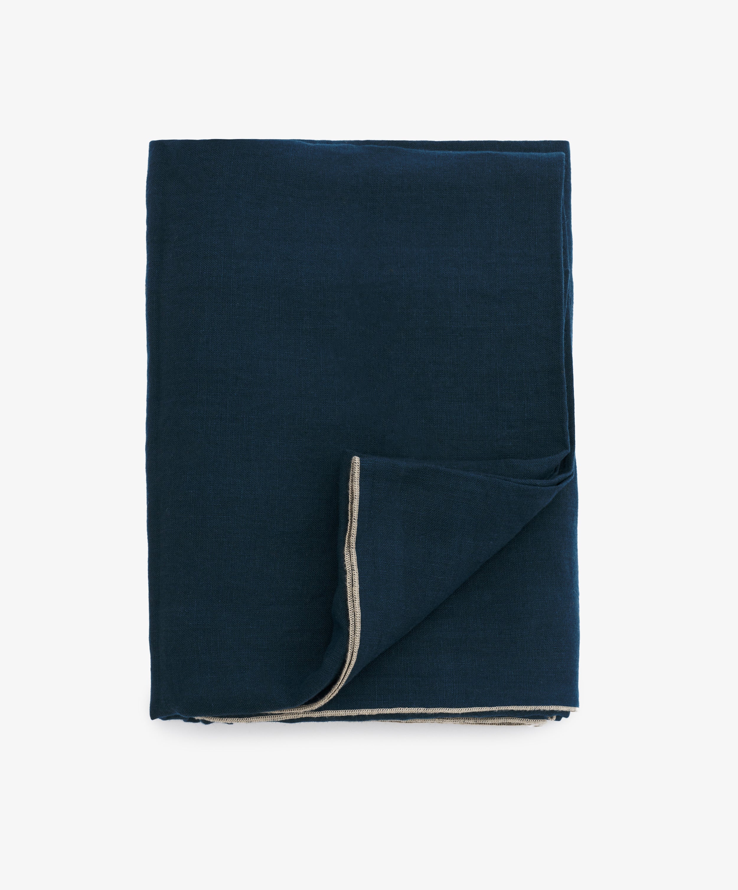 Venise Tablecloth. Folded dark blue linen cloth with cream stitched hem and bottom corner flipped up.