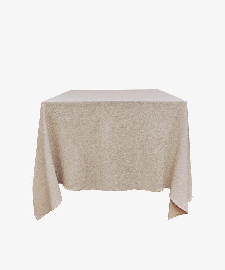 A square table draped with the Corte Tablecloth in plain beige, set against a white background.