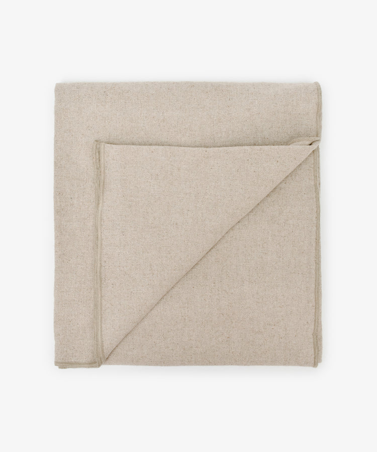The Corte Tablecloth, neatly folded in beige linen with a corner turned down, is displayed on a white background.