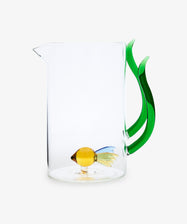 The Fish Pitcher is a hand-blown glass pitcher featuring a green seaweed handle and a small yellow glass fish at the bottom, adding ocean-inspired charm to your table.