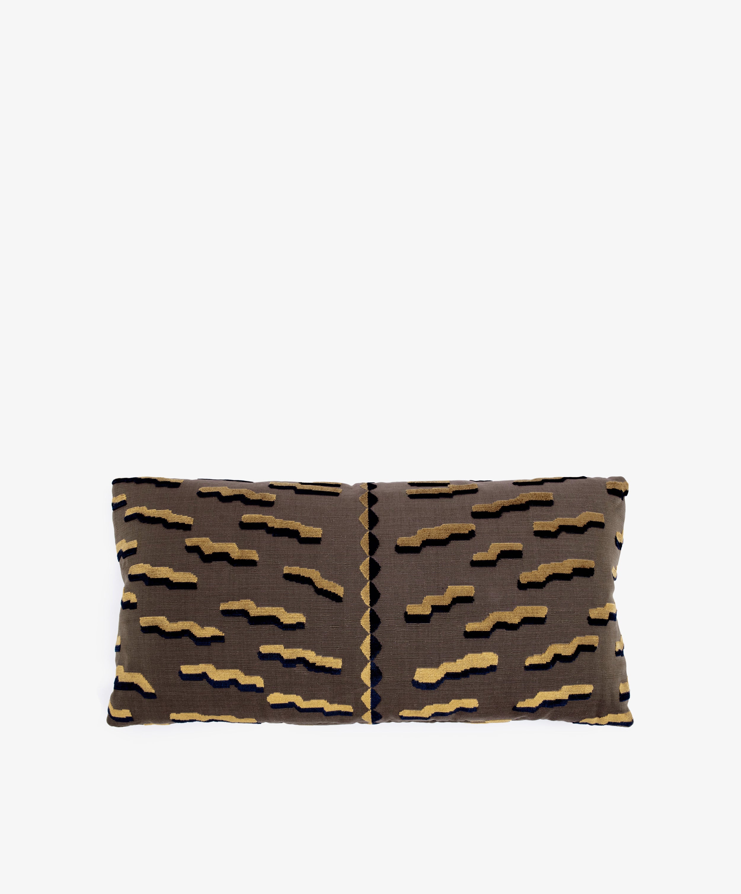 The Polo Lumbar Cushion is a rectangular pillow with a brown base and black, tan, and gold geometric zigzags, crafted from limited deadstock designer fabrics. Shown on a plain white background.