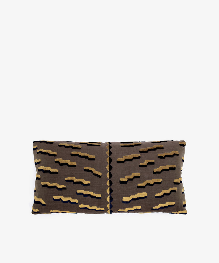 The Polo Lumbar Cushion is a rectangular pillow with a brown base and black, tan, and gold geometric zigzags, crafted from limited deadstock designer fabrics. Shown on a plain white background.