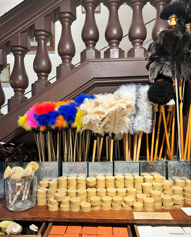 Display of colorful feather dusters, brushes, and stacked soaps in front of a wooden staircase