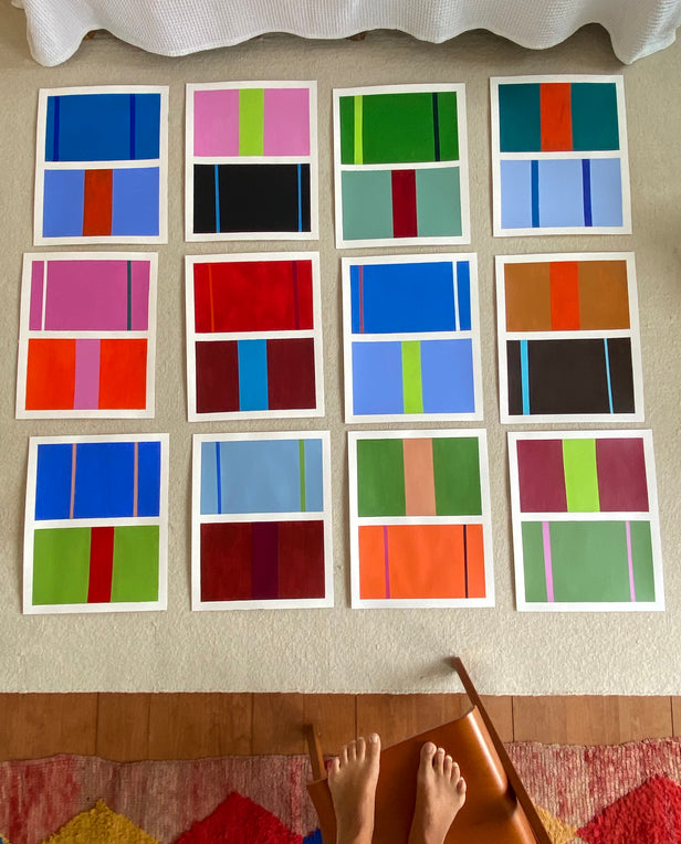 Series of colorful abstract prints arranged on the floor, viewed from above with feet visible at the bottom.