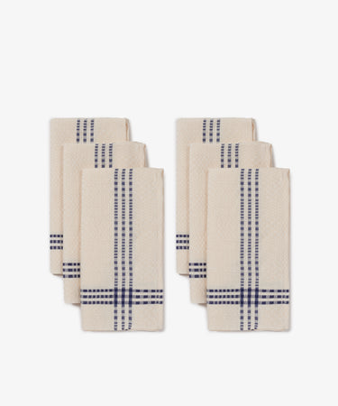 The Tilde Napkin, Set of 6, features beige napkins with blue plaid stripes in the classic Daldräll pattern, made from a cotton-linen blend and arranged in two neat stacks against a white background.