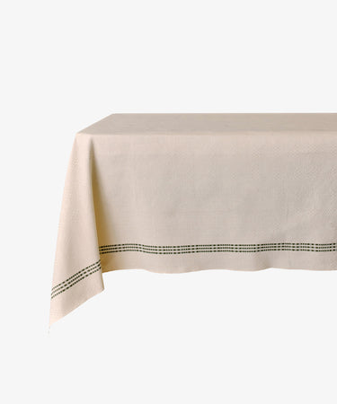 The Tilde Tablecloth is a rectangular Swedish design made from light beige cotton-linen, featuring a subtle texture and a simple black dotted border near the edge.