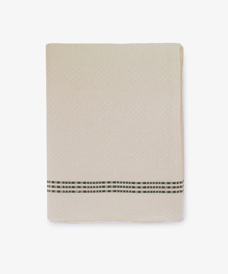 The Tilde Tablecloth, featuring a beige DaldrÃ¤ll weave and a black and white checked stripe near the edge, is neatly folded against a white background.