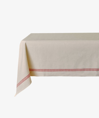 The Tilde Tablecloth, made from Swedish InsjÃ¶ns beige fabric with a red stitched border, is draped over a rectangular table set against a plain white background.
