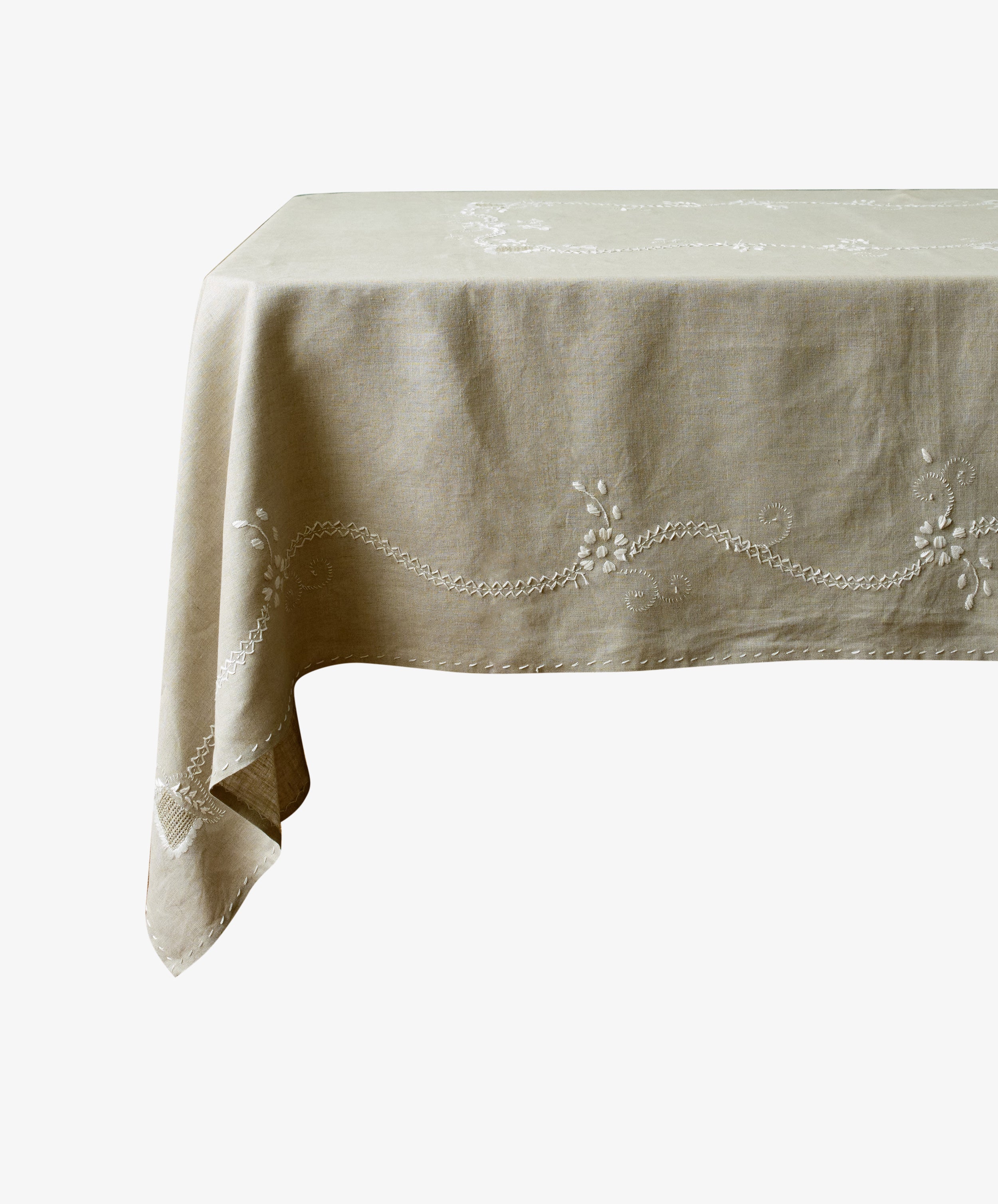 Zelia Tablecloth in natural linen with white embroidery details, draped over floating table.