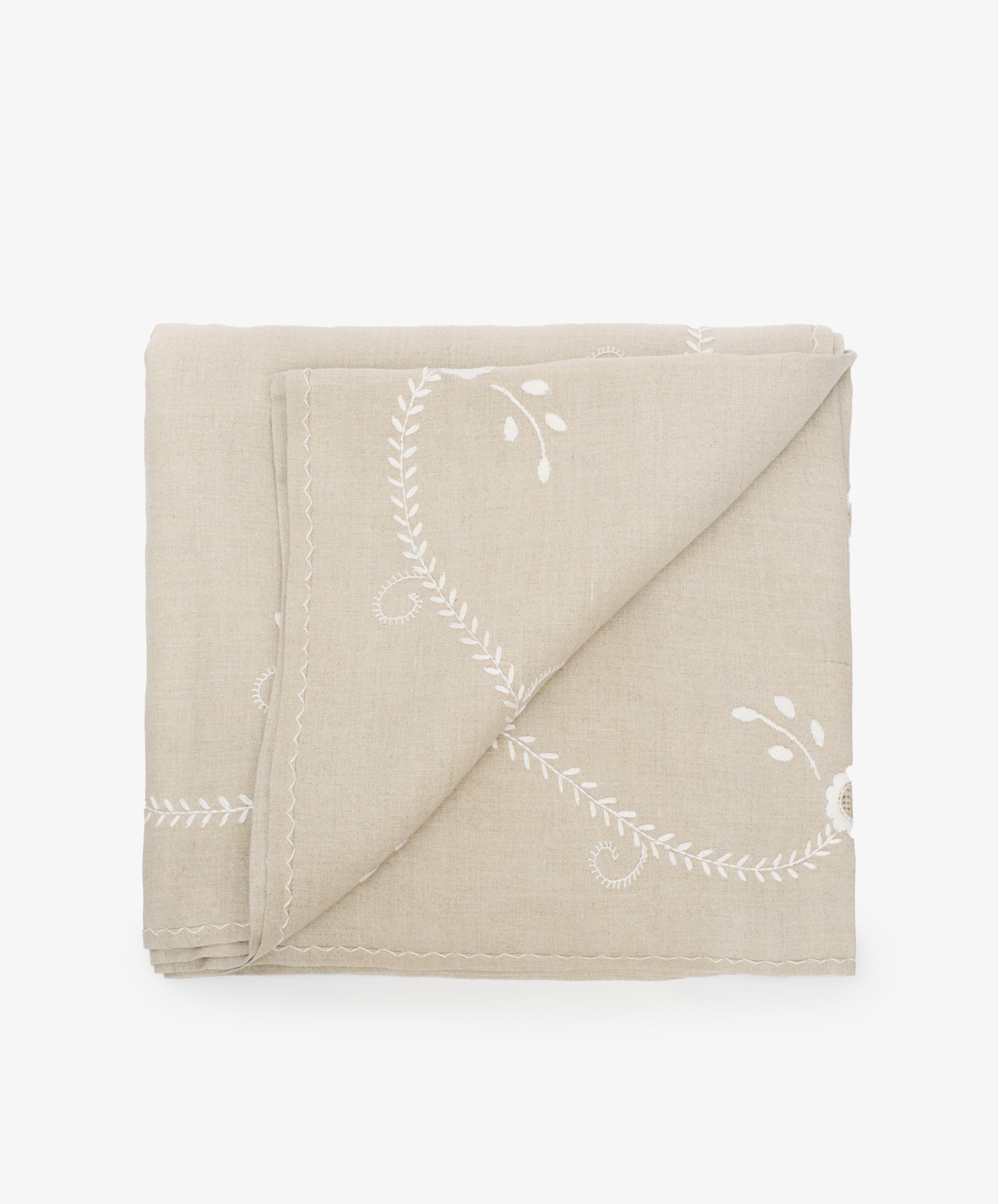 Zelia Tablecloth in natural linen with white embroidery details, folded with bottom corner flipped up.