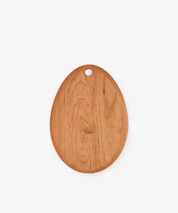 The Alden Egg Board, an oval-shaped cherry cutting board with a smooth finish and a small hole near one end, is photographed against a plain white background.