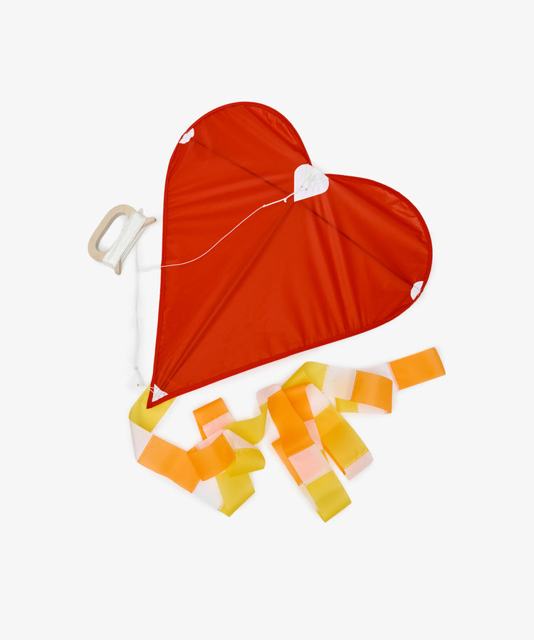The Love Supreme Kite is a red, heart-shaped kite featuring a handle and yellow-orange ribbon tail, shown on a white background—an ideal cheerful gift.