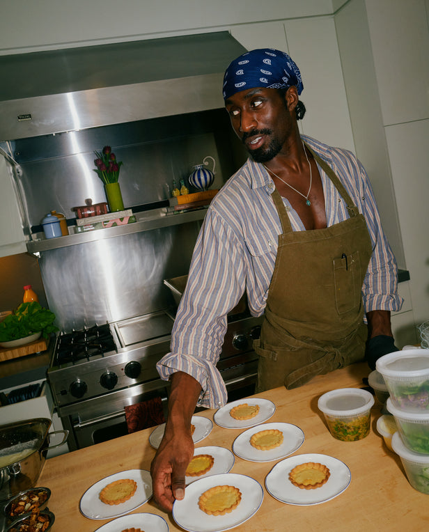 Person in a kitchen preparing food on a counter with plates of food.