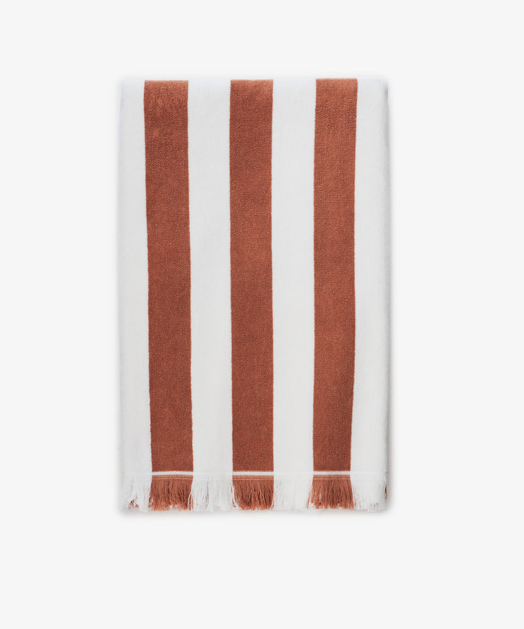 The Paloma Stripe Towel, crafted from striped cotton in bold brown and white verticals with a short white fringe along the bottom edge, evokes the relaxed elegance of the Italian coast.