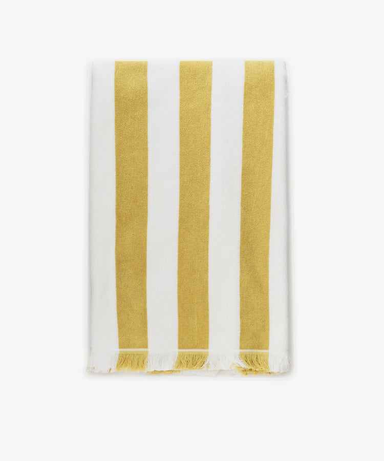 The Citrino Stripe Towel is a rectangular Italian beach towel featuring vertical yellow and white stripes with tasseled edges, shown neatly folded on a white background.