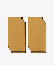 The Flavia Napkin set includes six mustard yellow linen napkins with black trim and double-line stitching, neatly stacked in two groups of three against a plain white background.