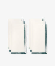 The Flavia Napkin Set of 6 features neatly folded linen napkins with dark green trim and a subtle double-line stitch, arranged in two groups of three on a plain white background.