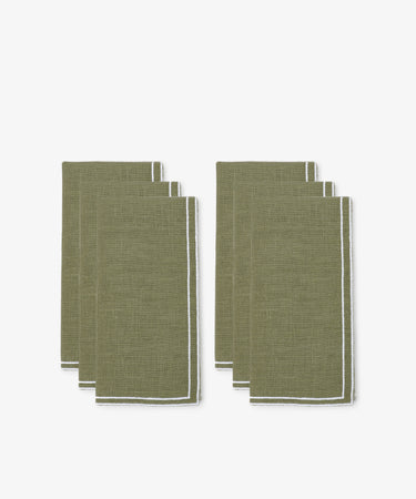 The Flavia Napkin, Set of 6, features olive green linen with white trim and double-line stitch. Neatly folded in two stacks on a white background, these napkins pair perfectly with Flavia placemats for an elegant table setting.
