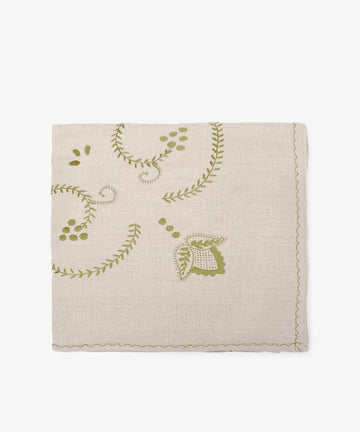 The Inez Tablecloth, crafted from Portuguese linen, is beige with green embroidered floral and leaf designs and finished with elegant scalloped edges.