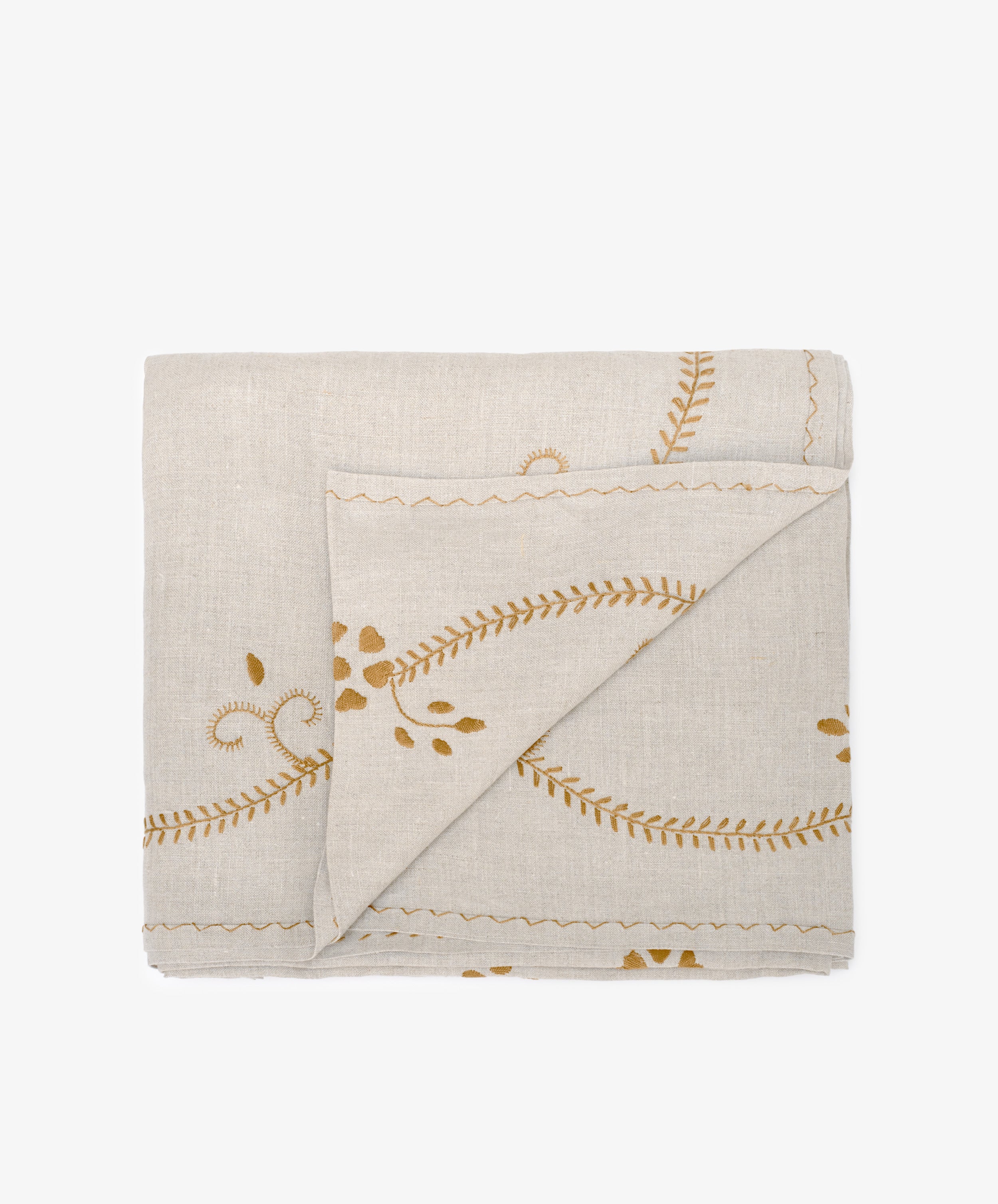 The Zelia Tablecloth is a folded beige linen piece with yellow embroidered leaf and vine patterns, echoing traditional Portuguese designs, displayed on a white background.