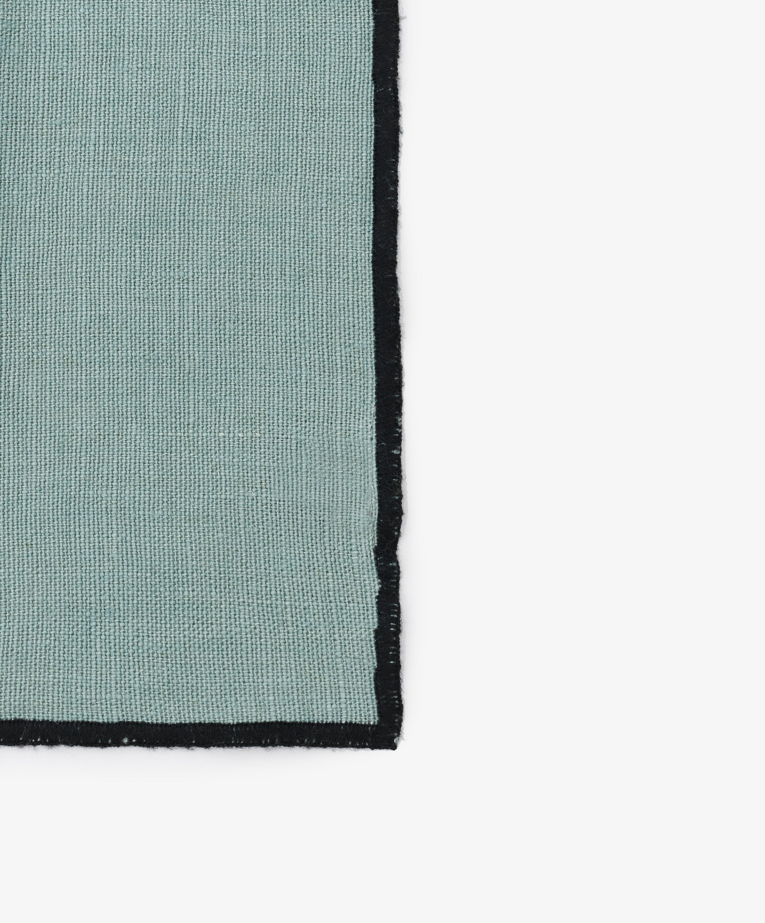 Close-up of black stitched edges on the celadon linen Luri Napkin.