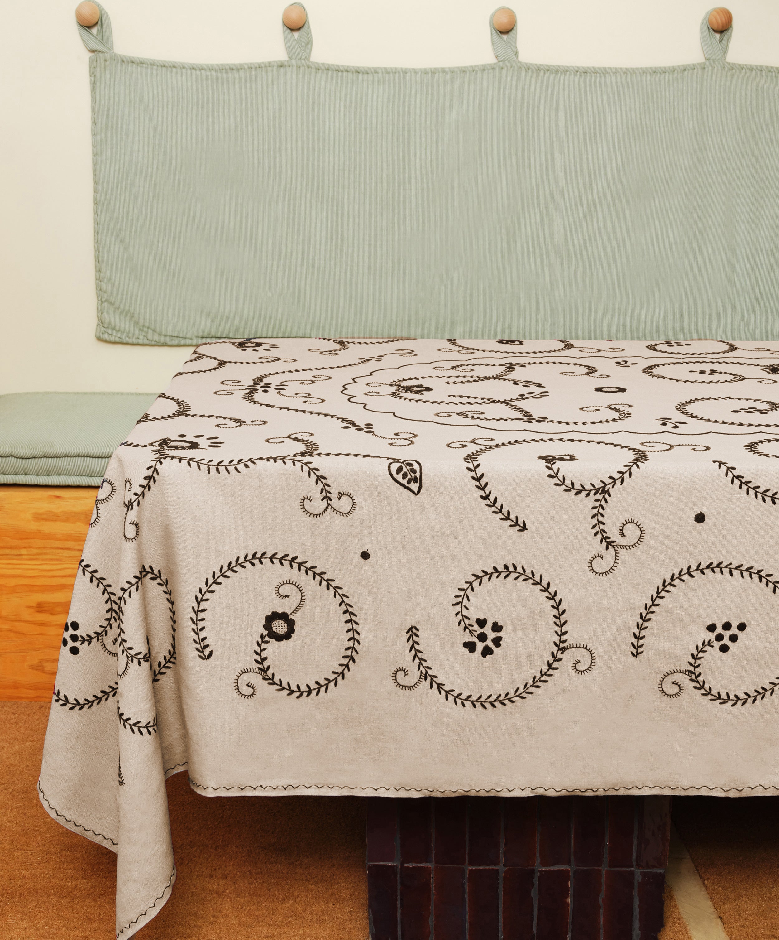 Tan and black Inez Tablecloth in situ, spread over table with green wall hanging and bench.