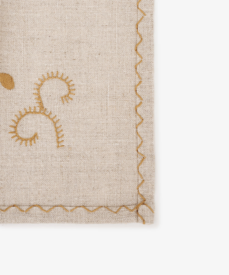 The Inez Napkin, Set of 6, features beige fabric with gold embroidered swirls and a scalloped stitched border on the right and bottom edges, inspired by traditional designs.