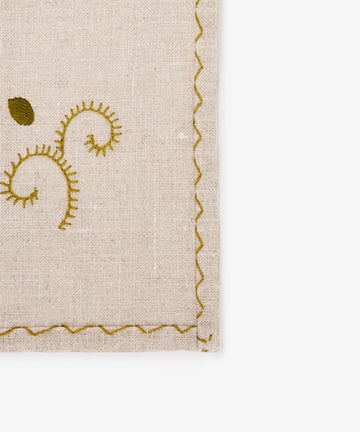 A close-up of the Inez Napkin, Set of 6, showcasing raw linen fabric with green hand-embroidered patterns and a scalloped green stitched border—an elegant touch for your table setting.