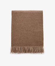 Folded Ulisse Throw in neutral beige merino wool with fringe detailing along the bottom edge, shown on a plain white background.