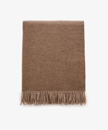 Folded Ulisse Throw in neutral beige merino wool with fringe detailing along the bottom edge, shown on a plain white background.