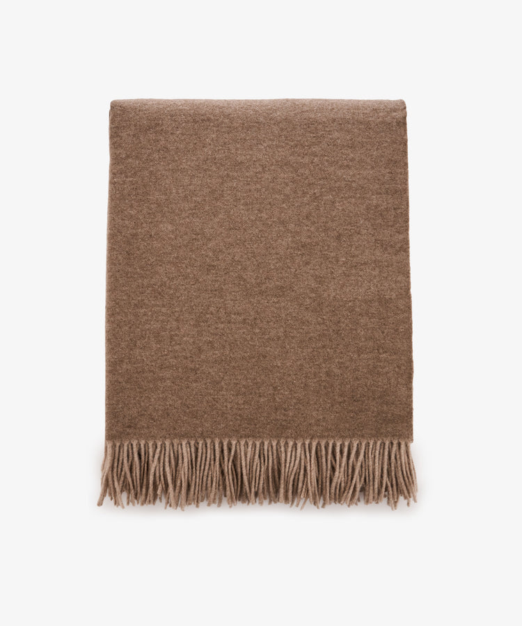 Folded Ulisse Throw in neutral beige merino wool with fringe detailing along the bottom edge, shown on a plain white background.
