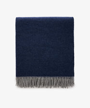 The Ulisse Throw, in oceanic blue with a gray fringe, is neatly folded and displayed against a plain white background.