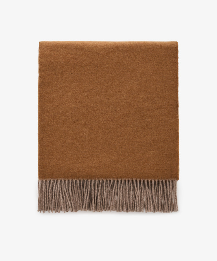 The Ulisse Throw, a folded brown wool piece with beige fringe detailing, is displayed on a plain white background.