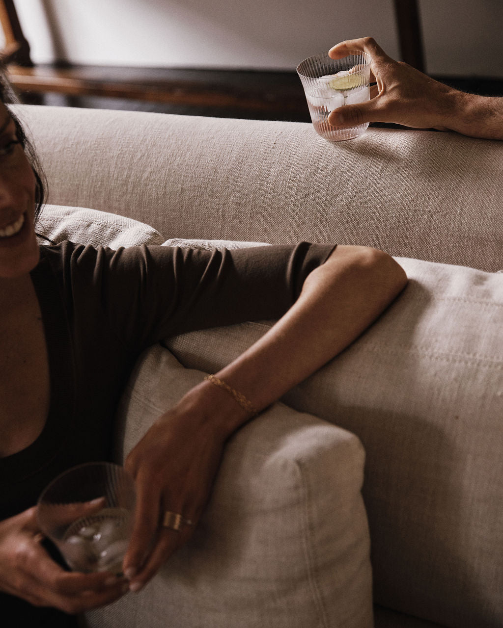 Two people, each holding a Linea Ribbed Tumbler filled with a drink and ice, relax on a beige couch.