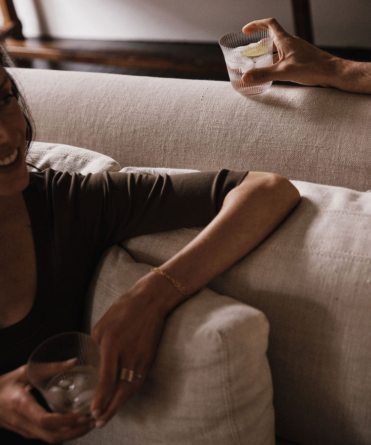 Two people, each holding a Linea Ribbed Tumbler filled with a drink and ice, relax on a beige couch.