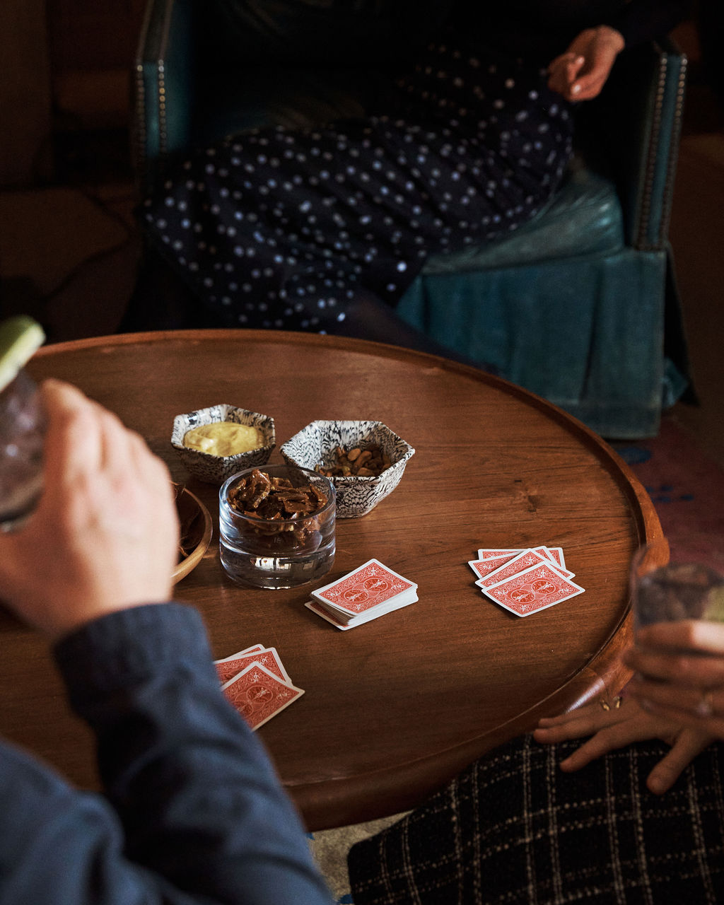 Three people sit around a wooden table with playing cards and drinks in hand, enjoying snacks served in the handcrafted Celine Snack Bowl.