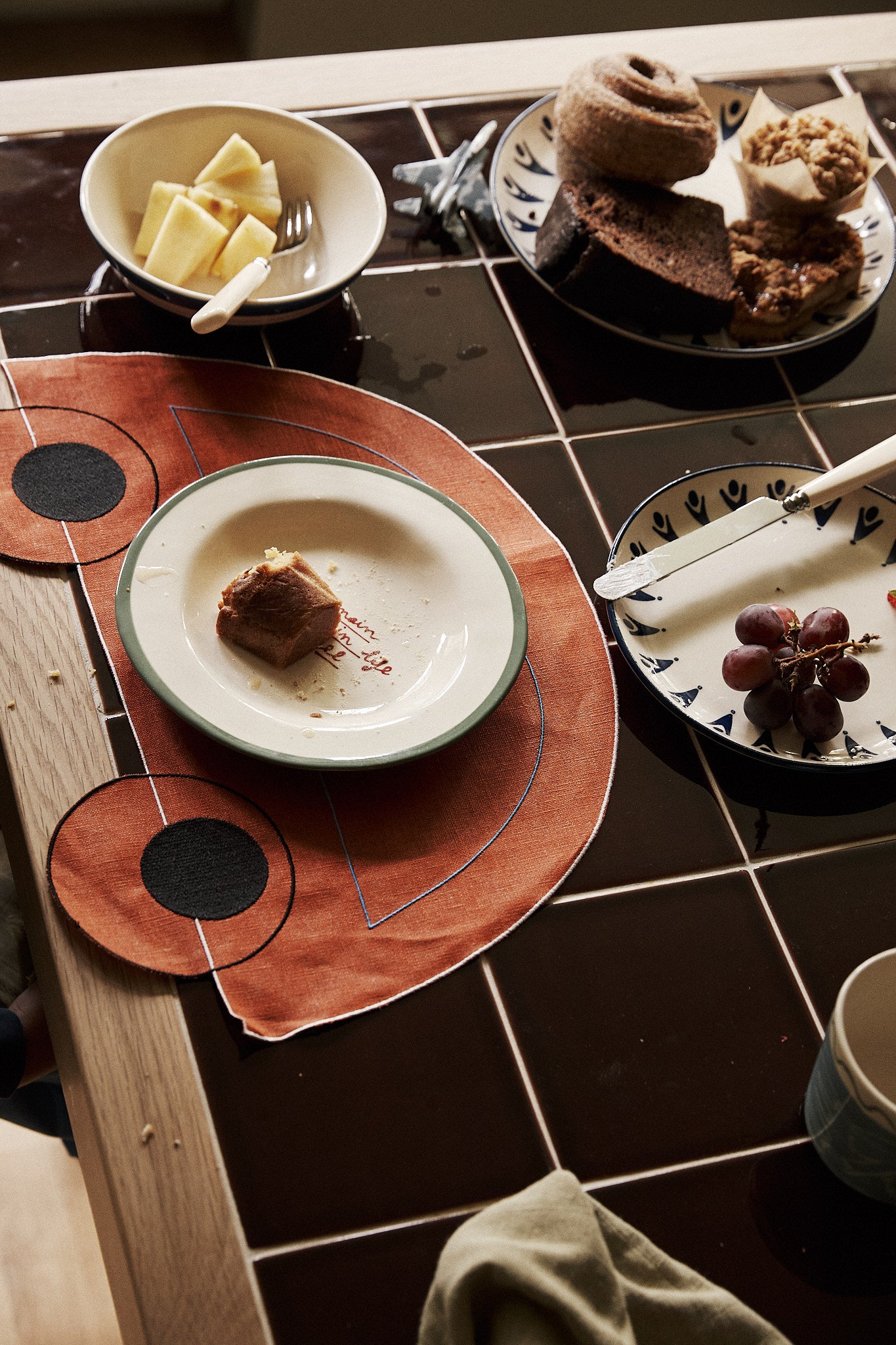 A table with plates of grapes, pineapple, assorted pastries, a fork, and a piece of cake served on Thomas Placemat, Set of 4.
