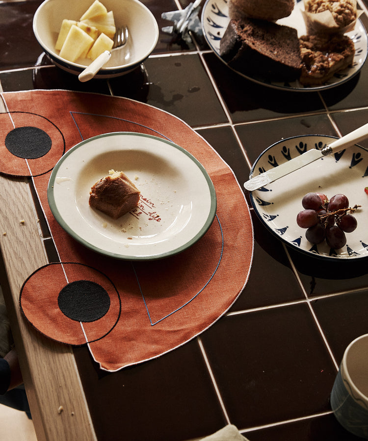 A table with plates of grapes, pineapple, assorted pastries, a fork, and a piece of cake served on Thomas Placemat, Set of 4.