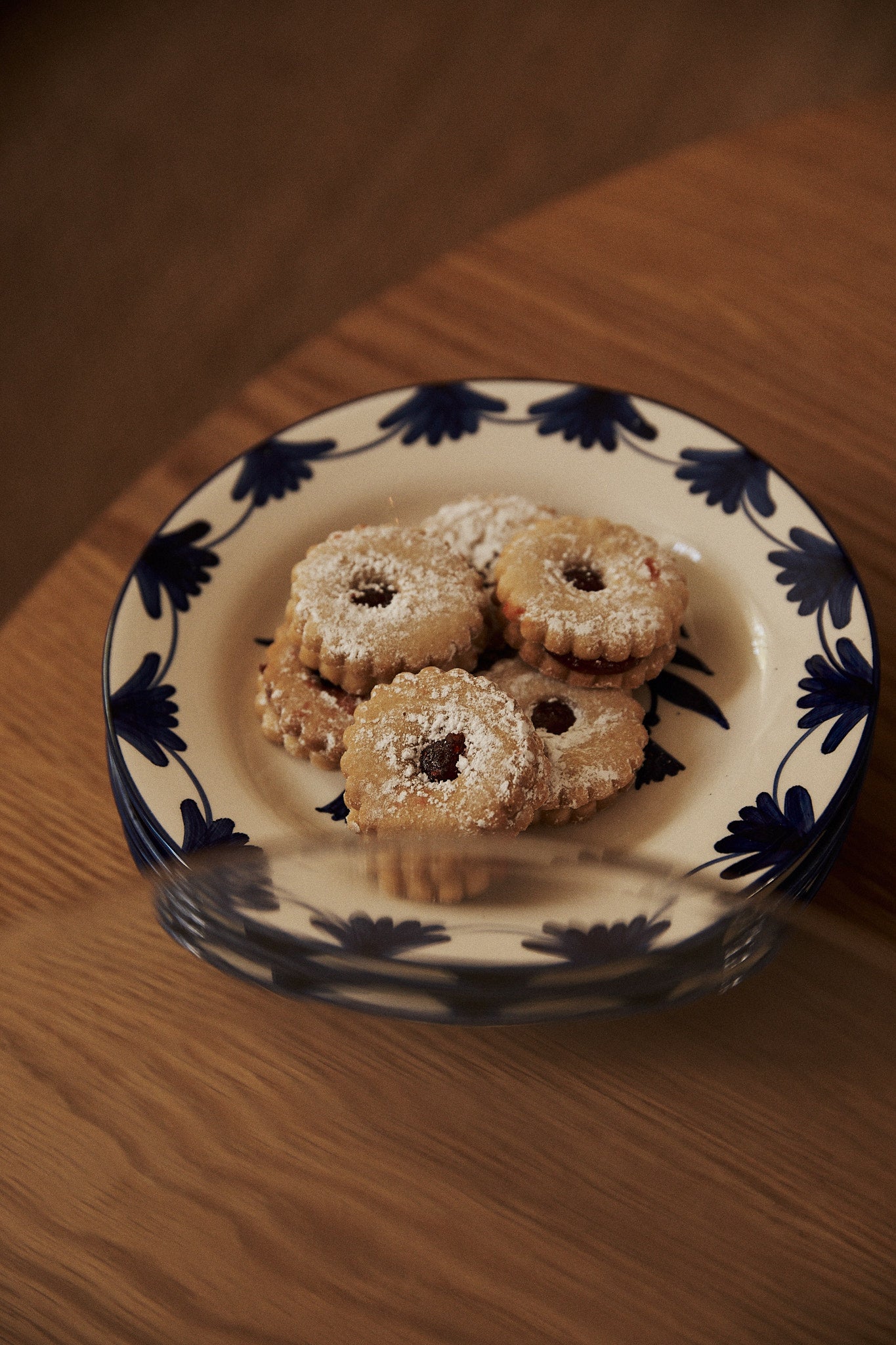 A Catalina Small Plate from the set of 4, inspired by Portuguese ceramics, holds five round, jam-filled cookies dusted with powdered sugar and rests on a wooden surface.