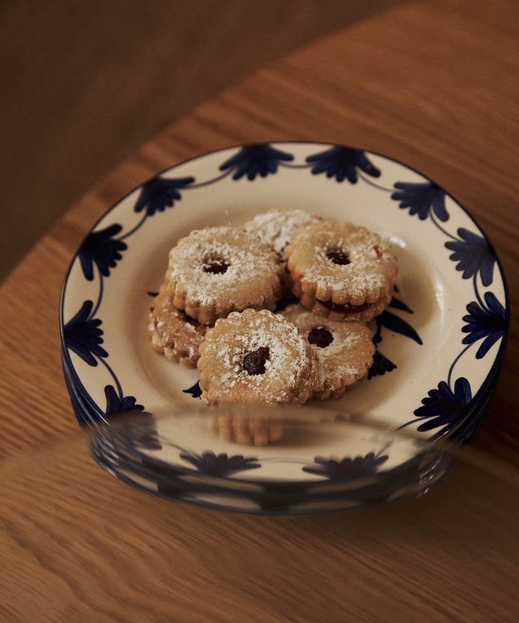 A Catalina Small Plate from the set of 4, inspired by Portuguese ceramics, holds five round, jam-filled cookies dusted with powdered sugar and rests on a wooden surface.