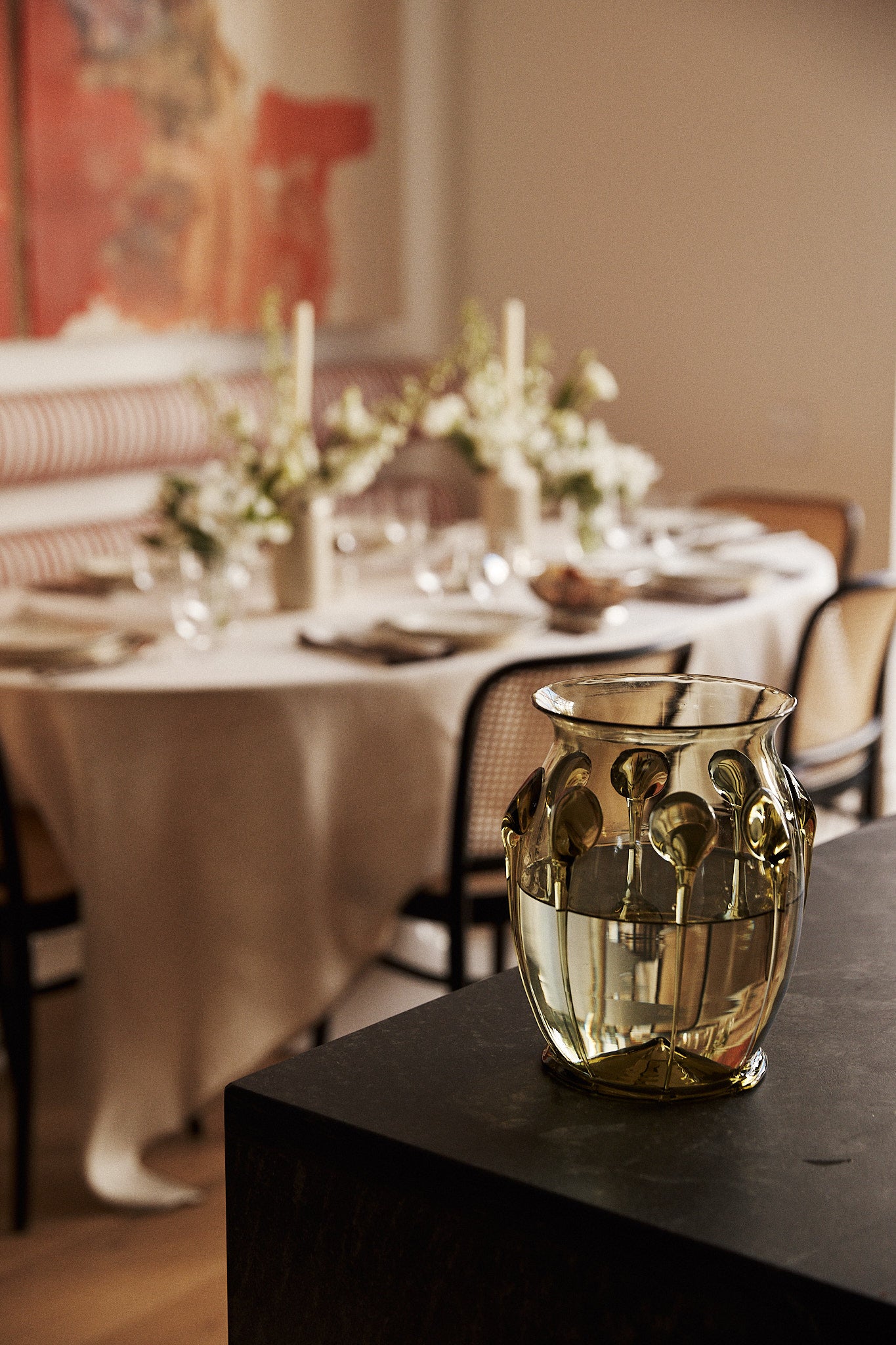 A textured, translucent gold glass vase with a floral pattern sits on a dark table in a softly blurred dining room setting.