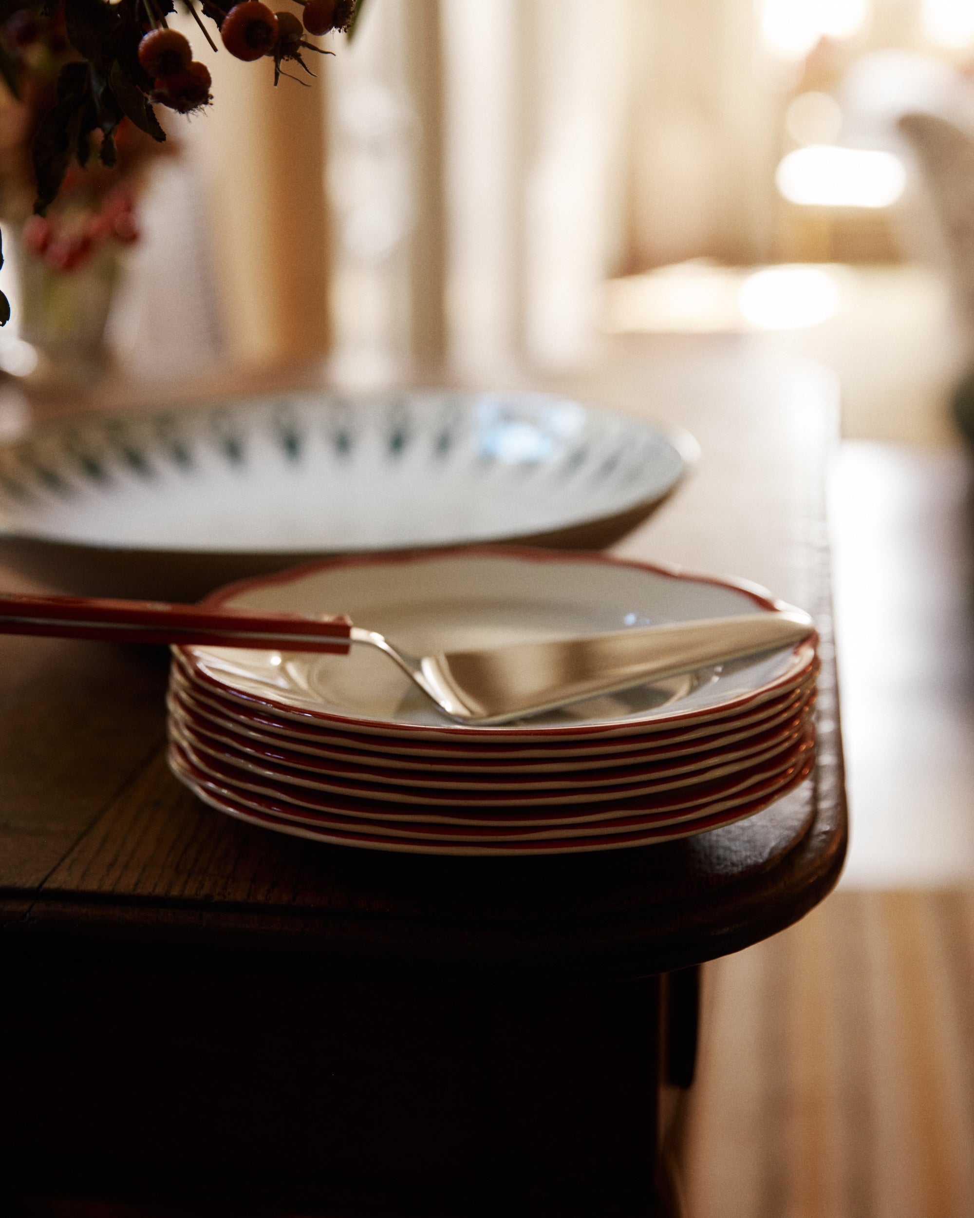 A stack of small plates, a Tart Server, and a fork sit on a wooden table next to a large serving bowl.