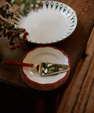 A stack of Petalo Small Plate, Set of 4 sits next to a large Bitossi Home Italian ceramic scalloped plate on a wooden table, topped with a pie server.