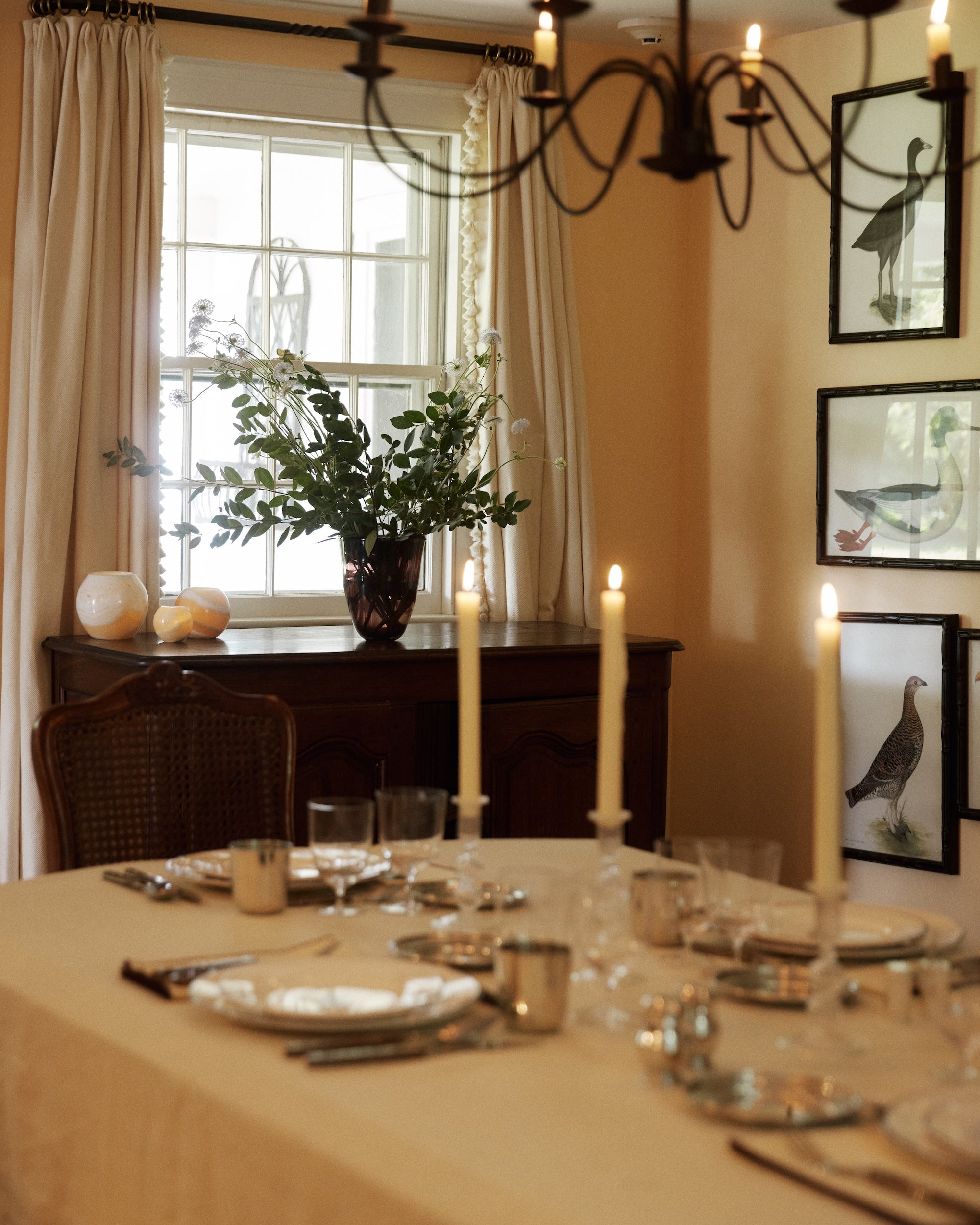 A dark plum Aura Vase holding green stems and white flowers, placed on a wooden sideboard behind a candlelit dining table.