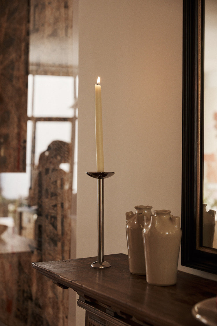 Candle in a holder on a wooden surface with decorative vases and a mirror in the background.